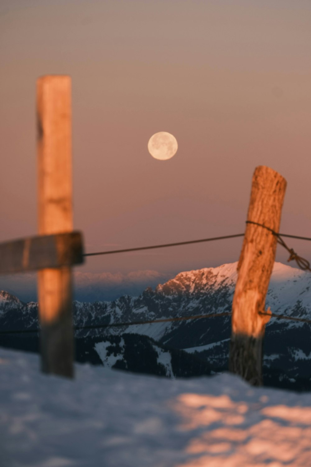 the moon is setting over a snowy mountain range