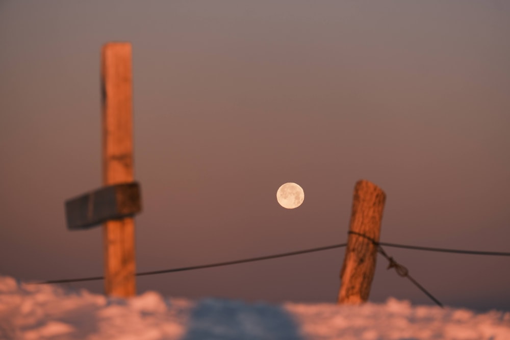 a full moon is seen behind a wooden post