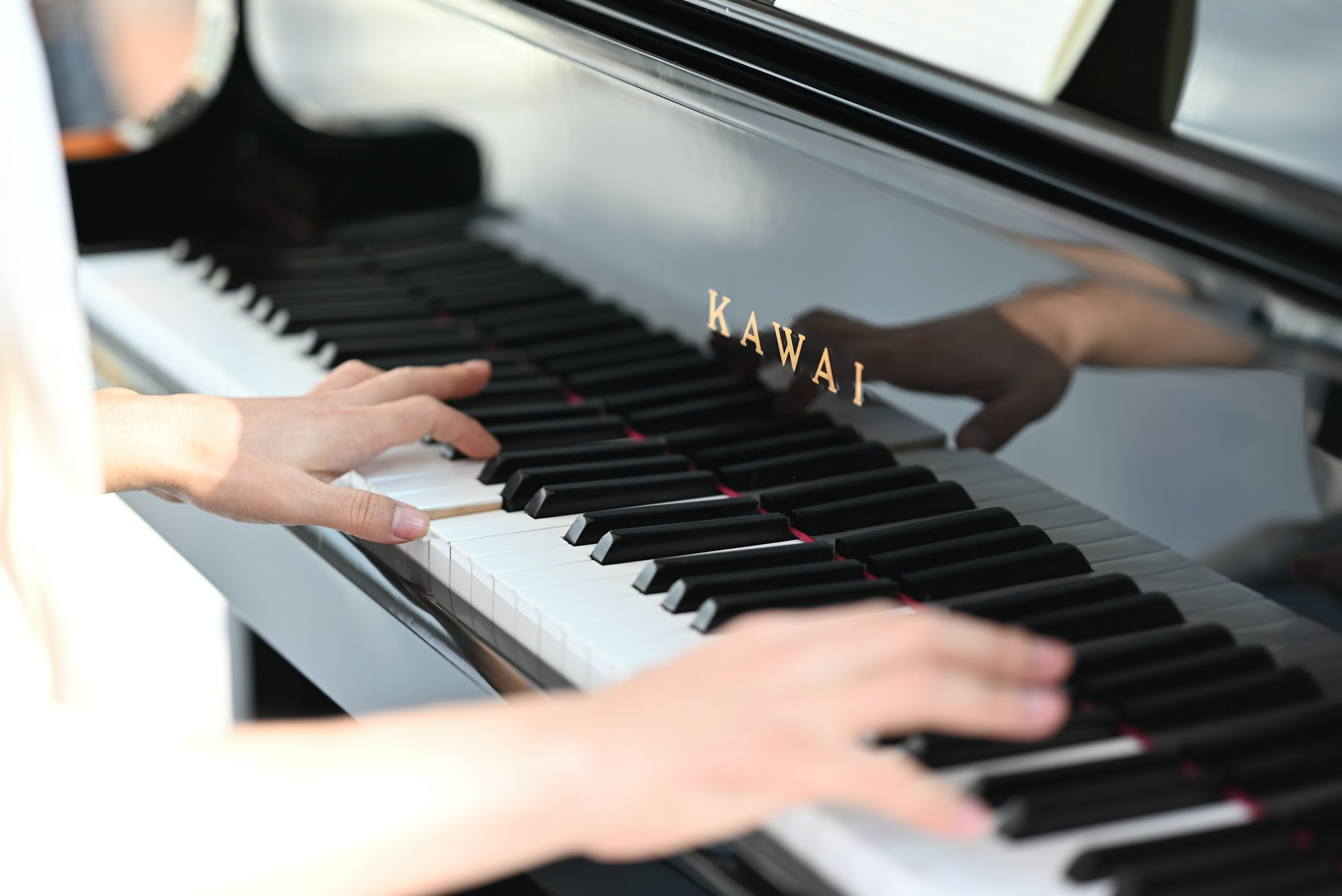 Hands playing grand piano keyboard with brand KAWAI.