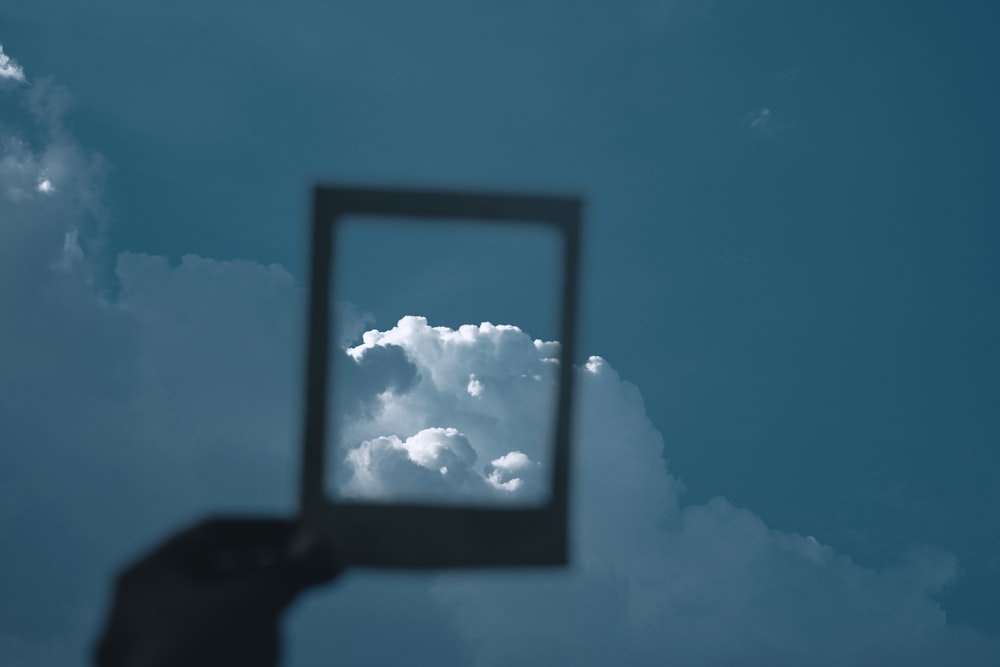 a hand holding up a square mirror in the sky