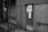 An industrial building features a corrugated metal wall with a fire exit door. Signs warn of required eye protection and emphasize keeping the fire exit clear. A ladder is attached to the wall, and there is a warning sign indicating danger.