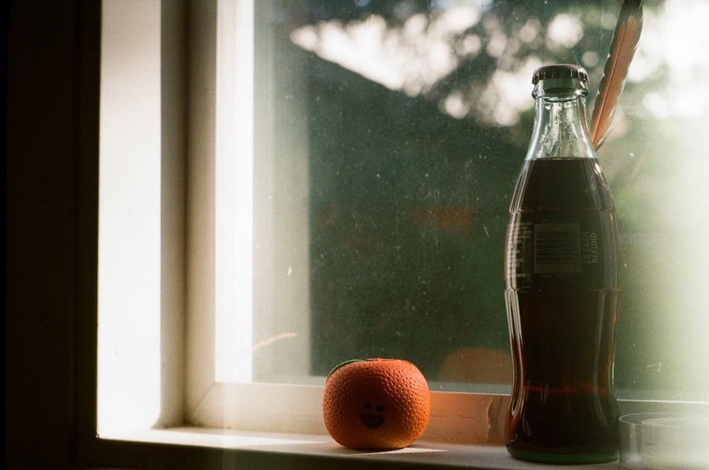 an orange sitting on a window sill next to a bottle