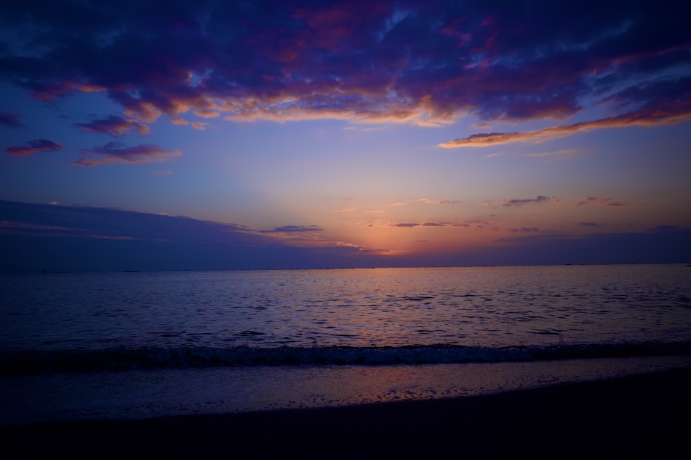 the sun is setting over the water on the beach