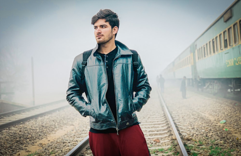 a man in a leather jacket standing in front of a train