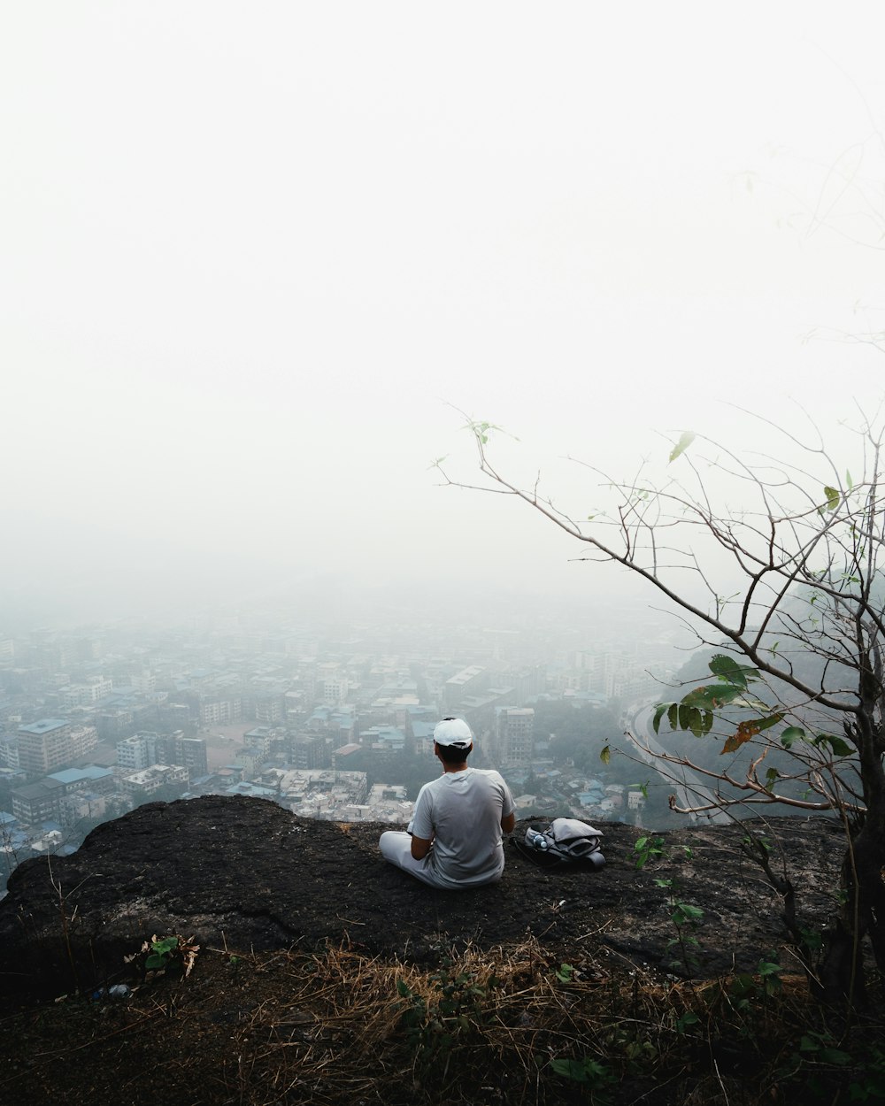 a man sitting on top of a hill next to a tree