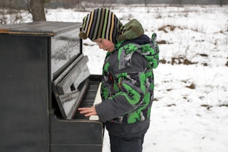 a young boy playing a piano in the snow