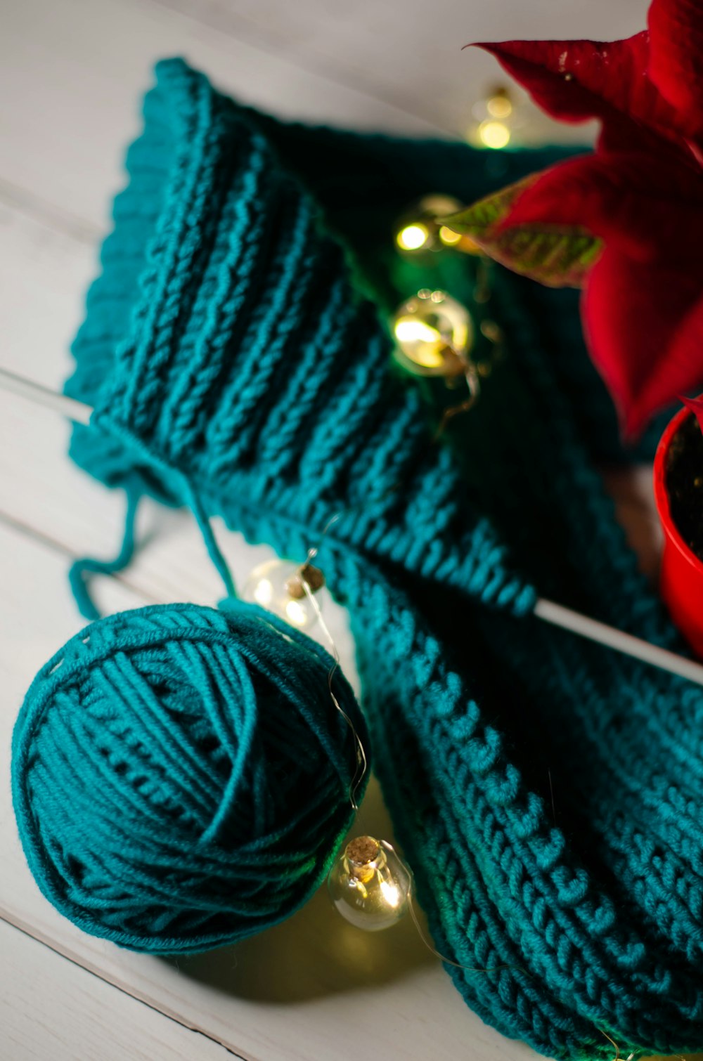 a green knitted scarf with a red vase of flowers