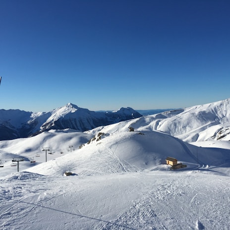 Snow-covered ski hill with luxury chalets in the background under clear blue sky.