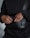 A person wearing a black sweatshirt is seen with their hands inside a small black bag with a shoulder strap. The bag has a logo printed on it.