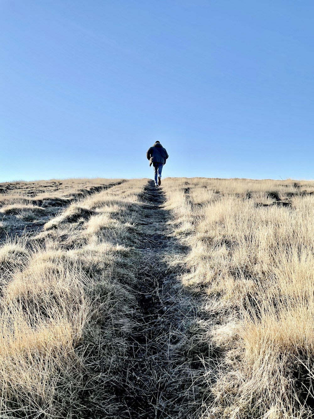 a man walking across a dry grass covered field