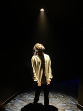 Portrait of Uday Harish bathed in warm spotlight on a dark stage, capturing a thoughtful, playful expression.