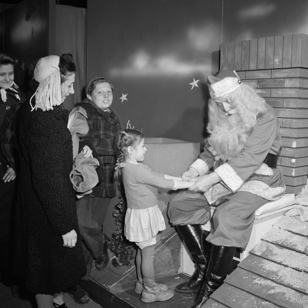 a black and white photo of a santa clause shaking hands with children