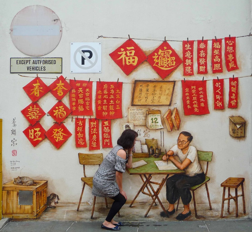 a man and a woman sitting at a table in front of a wall with chinese