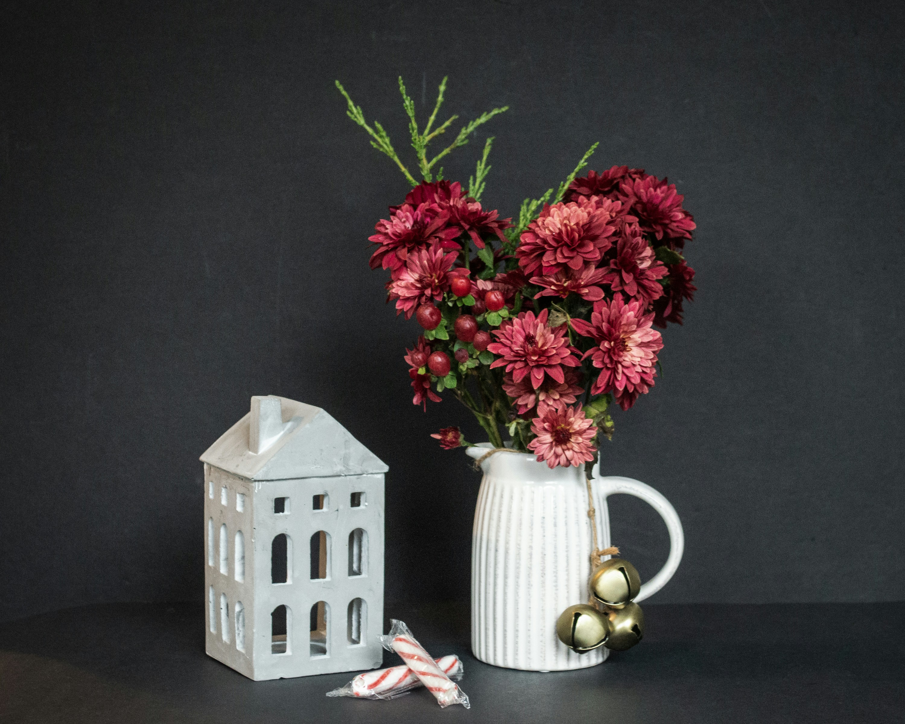 a white vase filled with red flowers next to a white house
