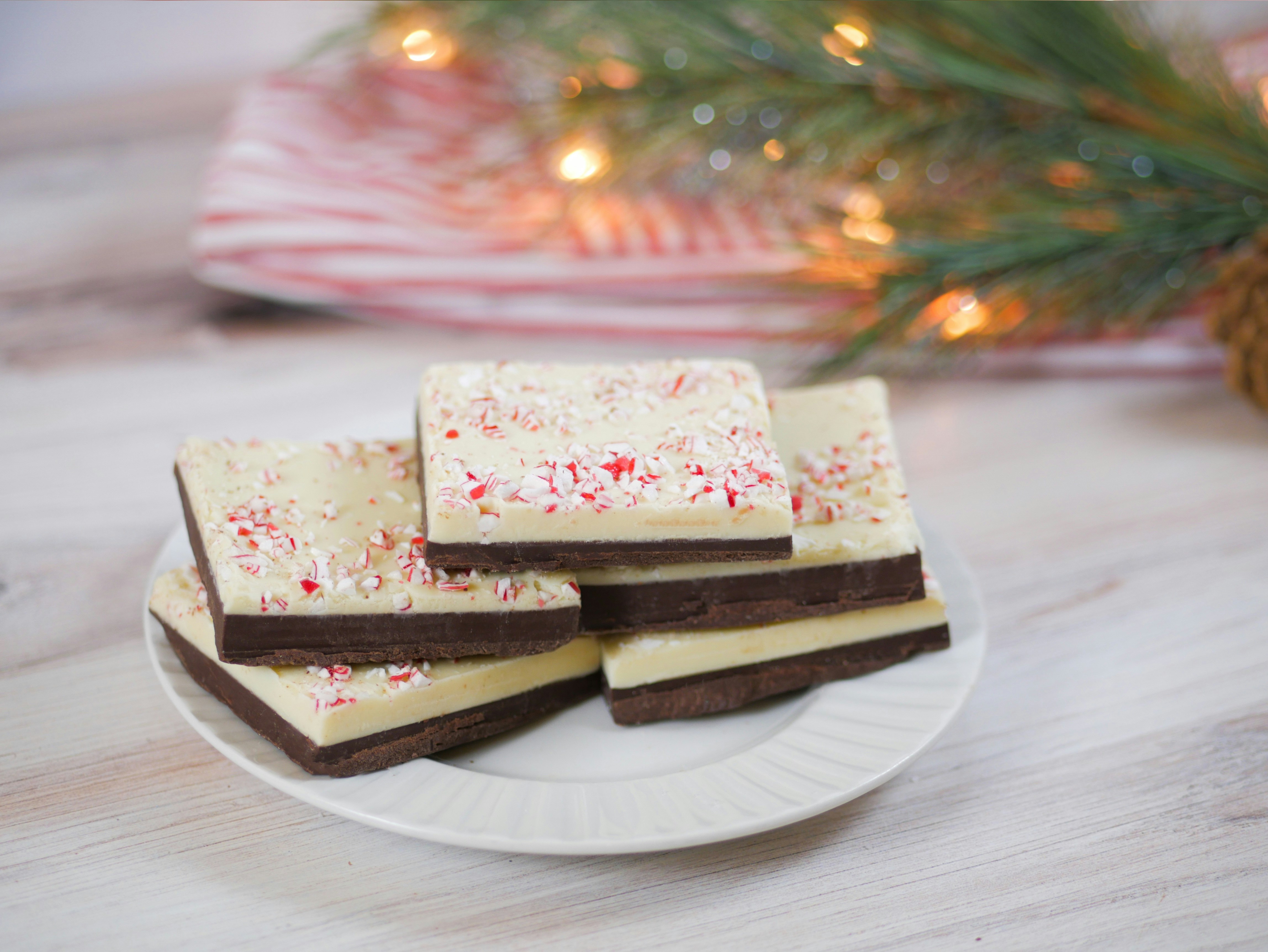 Dark and white chocolate peppermint bark pieces in a kraft paper box with candy cane pieces, festive flat lay