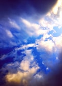 A dynamic view of the sky filled with vibrant clouds. The contrast between dark and light areas creates a dramatic effect, with vivid blue and softer hues blending beautifully.