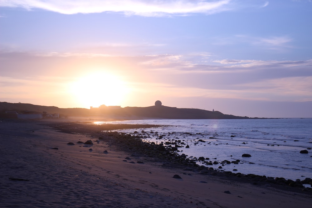 the sun is setting over the ocean on the beach