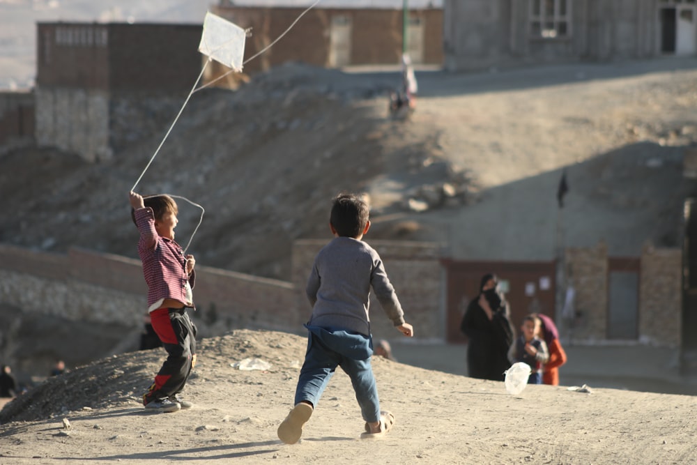 a couple of kids flying a kite on top of a hill