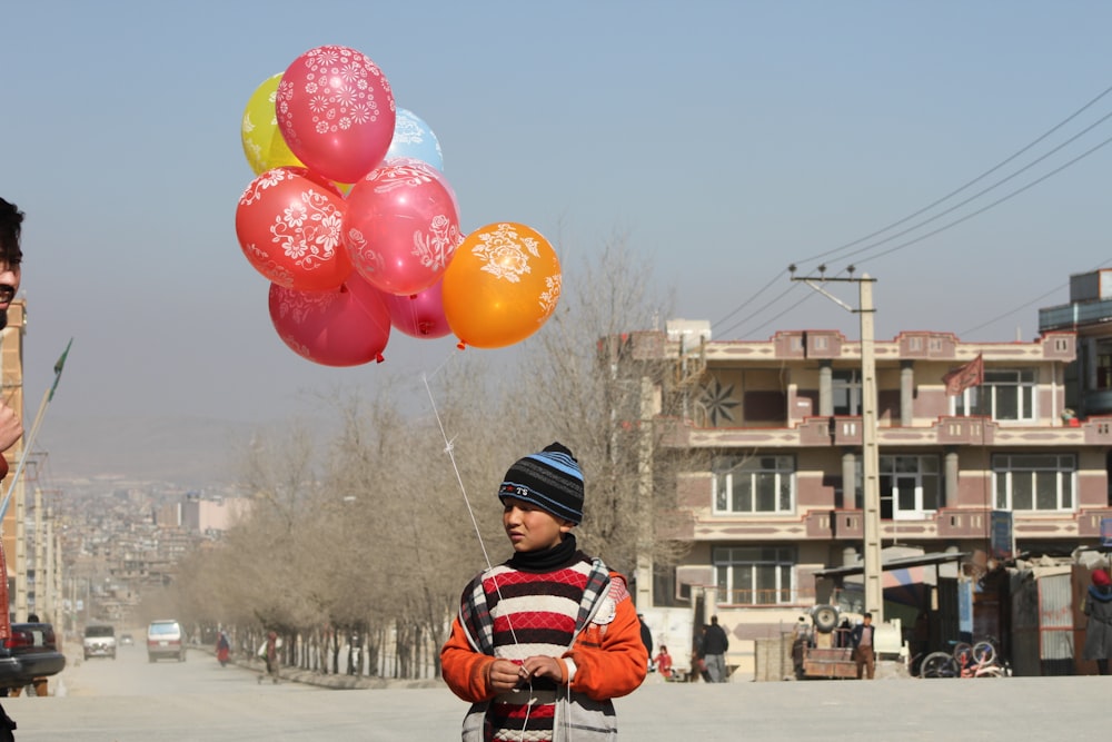 a young boy holding a bunch of balloons