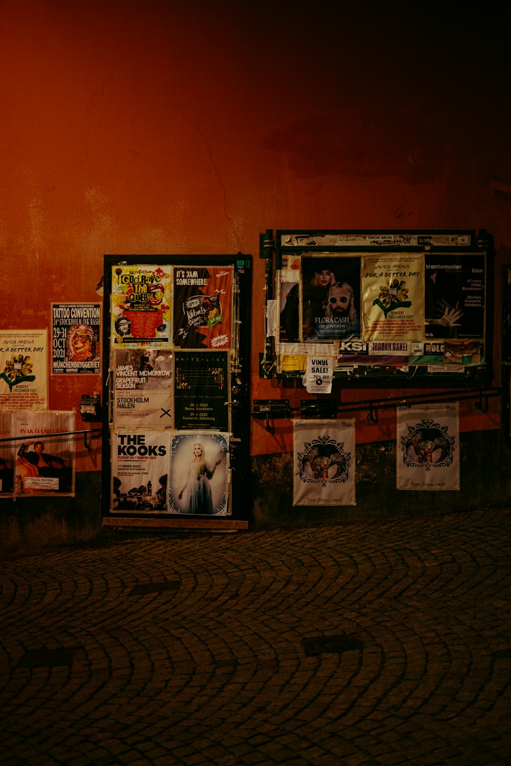 a wall covered in posters next to a sidewalk