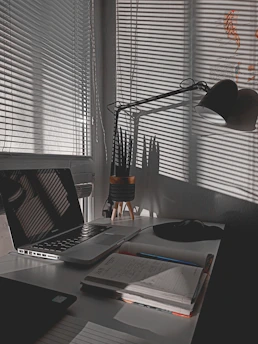 A cozy workspace with a laptop, notebook, and a cup of coffee beside a small plant, bathed in warm natural light.