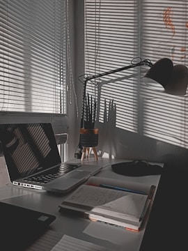 Creative workspace with notebooks, laptop, and green plants under soft lighting.