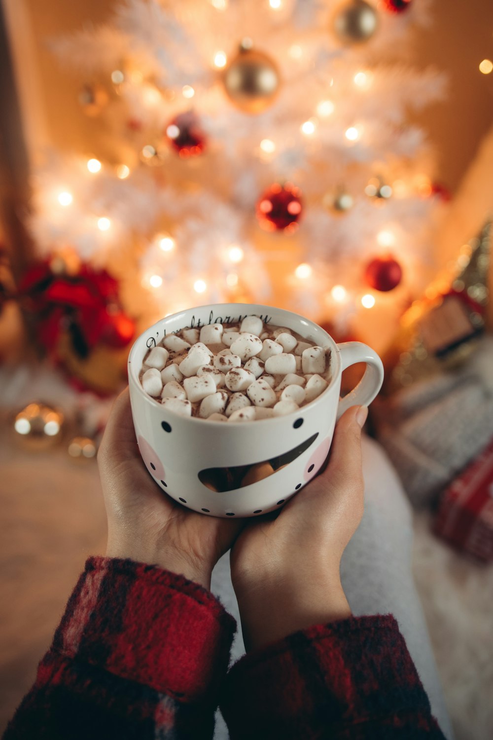 a person holding a cup of hot chocolate in front of a christmas tree