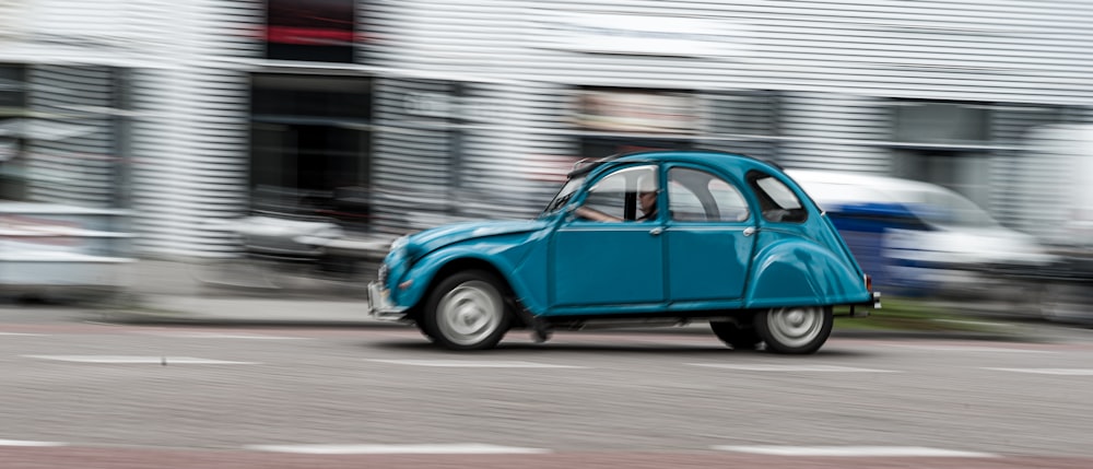 a blue car driving down a street next to a building