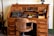 An antique wooden roll-top desk featuring a vintage typewriter and early office equipment. The desk has multiple small drawers and compartments, with a large wooden chair positioned in front. Additional items on the desk include an old telephone, inkwells, and paper.