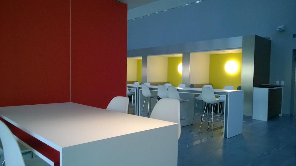 a room filled with white tables and chairs next to a red wall