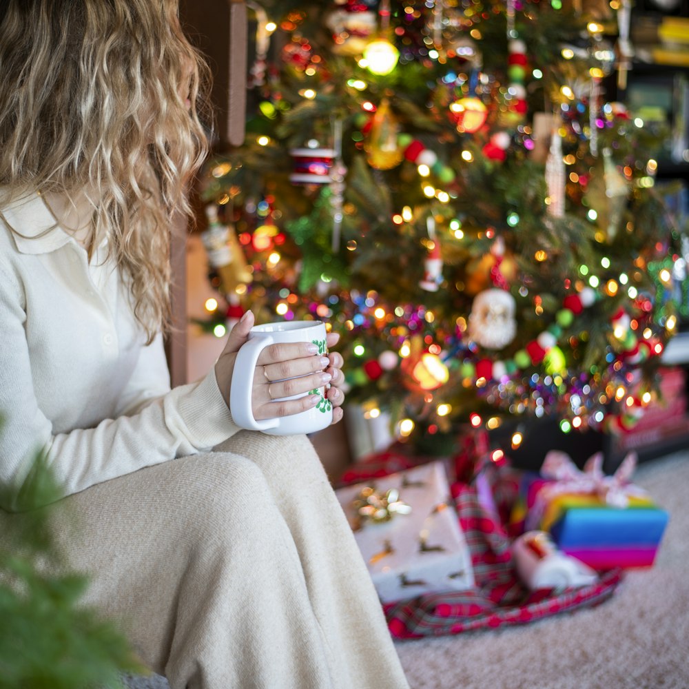 a woman sitting in front of a christmas tree holding a cup