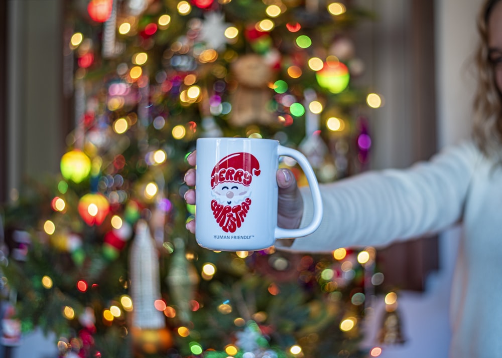 a woman holding a coffee mug in front of a christmas tree