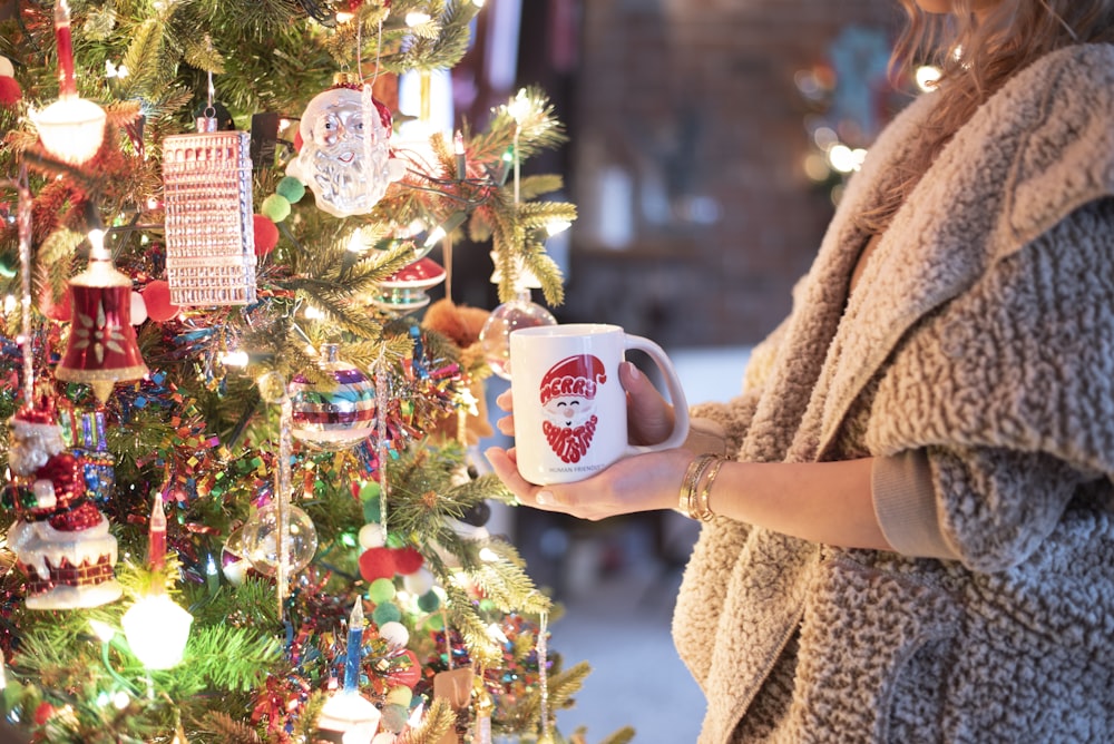 a woman holding a coffee mug in front of a christmas tree