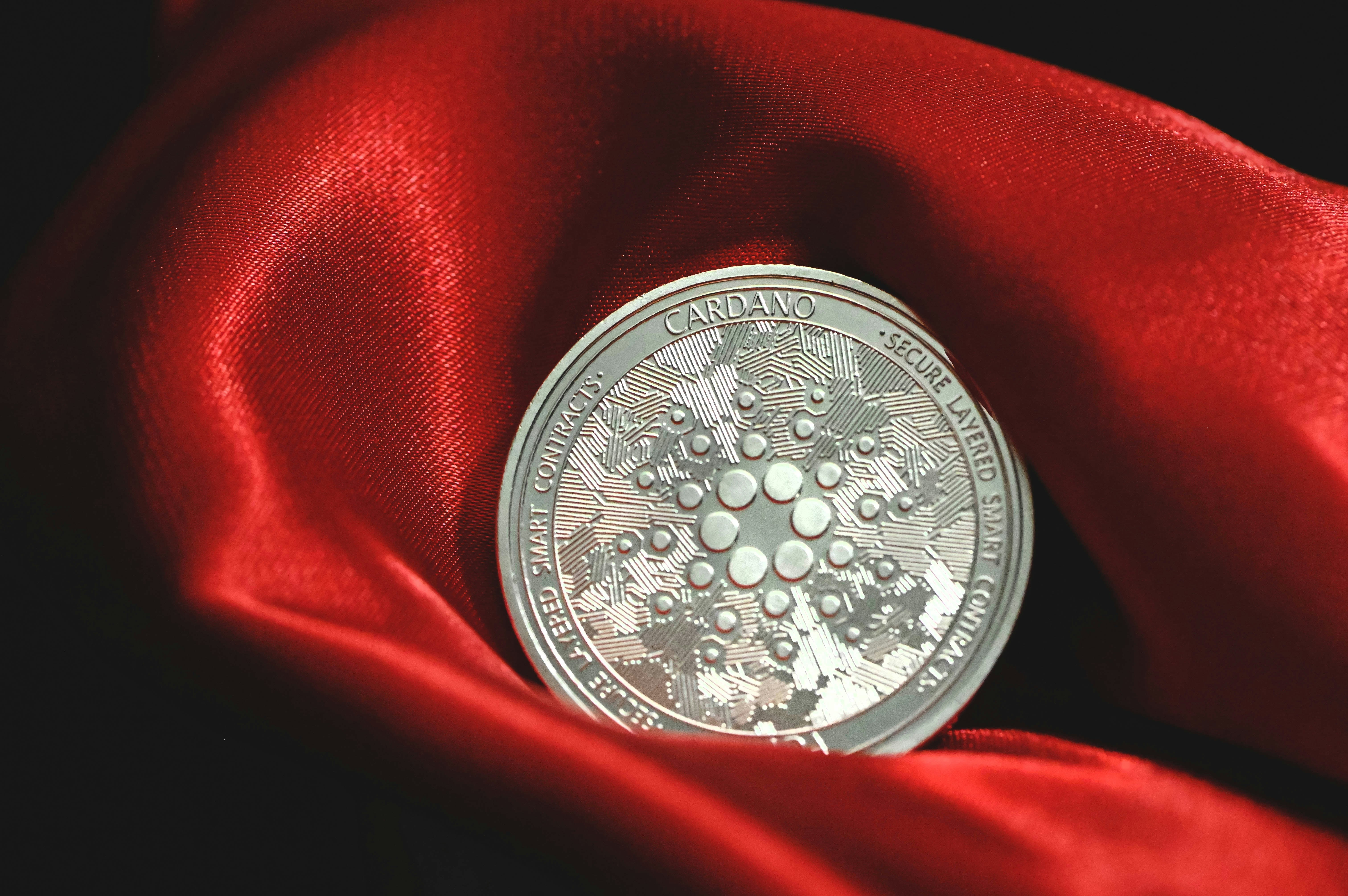A silver Cardano coin on top of a red velvet