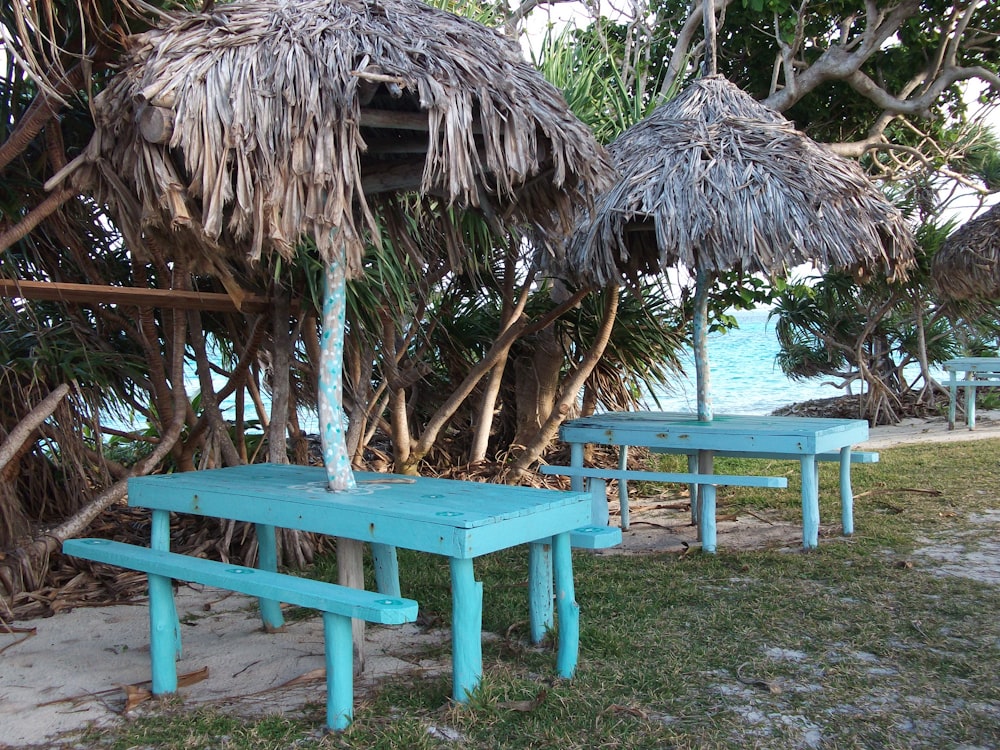 a couple of blue benches sitting under a thatched umbrella