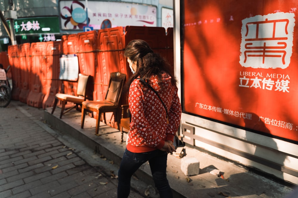 a woman walking down a street past a red sign