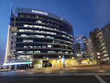 Modern glass office building exterior glowing at dusk with warm lights.