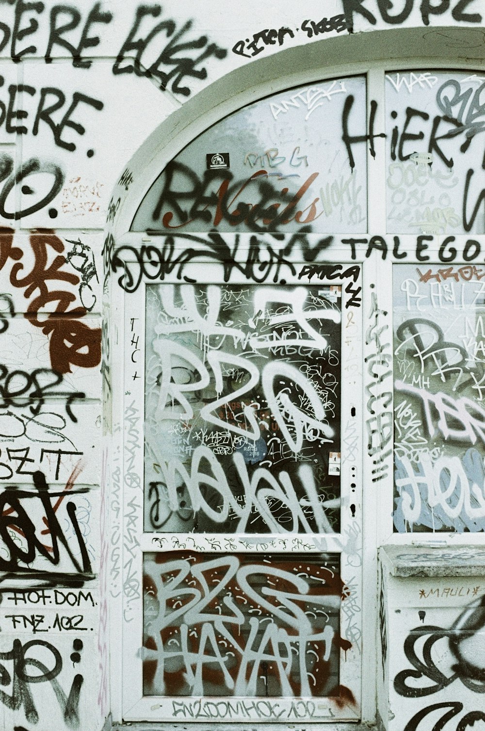 a window covered in lots of graffiti next to a wall