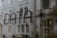Text formed by small dots spelling the word 'DATA' followed by an asterisk, seen on a glass surface with a blurred building in the background.