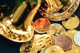 A collection of various cryptocurrency coins are scattered, including prominent ones like Ethereum and Bitcoin, surrounded by decorative golden objects.