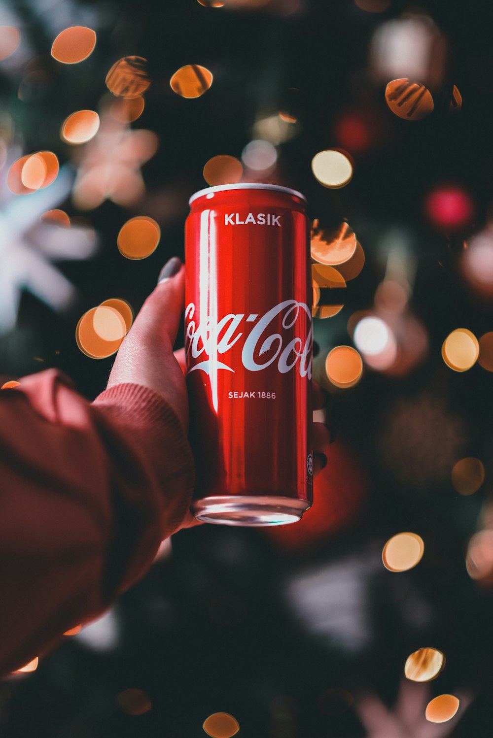 a person holding a can of coca cola in front of a christmas tree