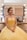 A woman dressed in an elegant yellow gown sits in a brightly lit makeup room. Her hair is styled with colorful flowers, and she looks content. A makeup station with various cosmetics is visible in the background.