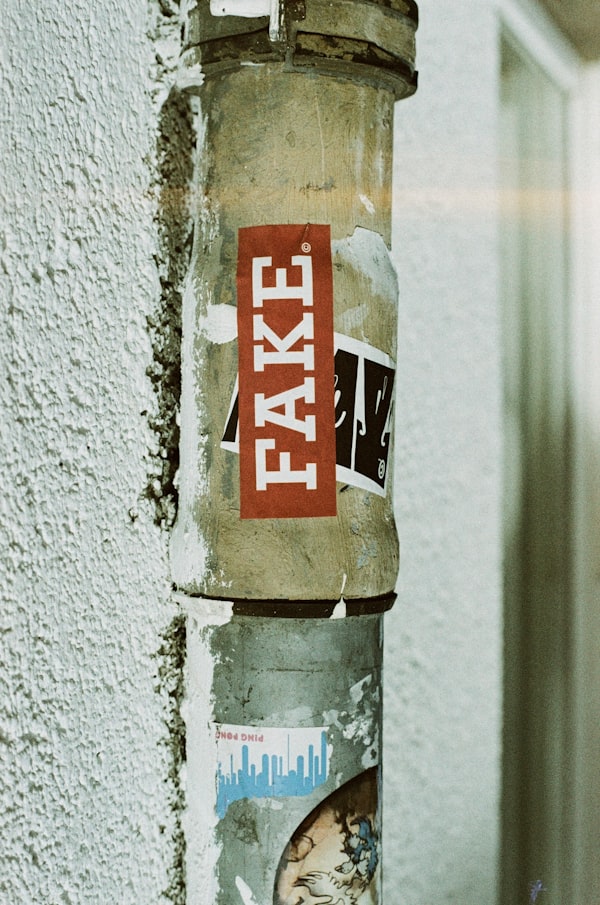 Foto de una tubería en un muro con stickers encima. Uno de ellos dice fake. ¿Por qué? Ni idea.