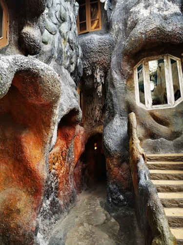 A structure resembling elements of natural rock formations with windows and an entryway, featuring textured surfaces in vivid earthy colors. The setting resembles a cave with irregular shapes and a small stairway.
