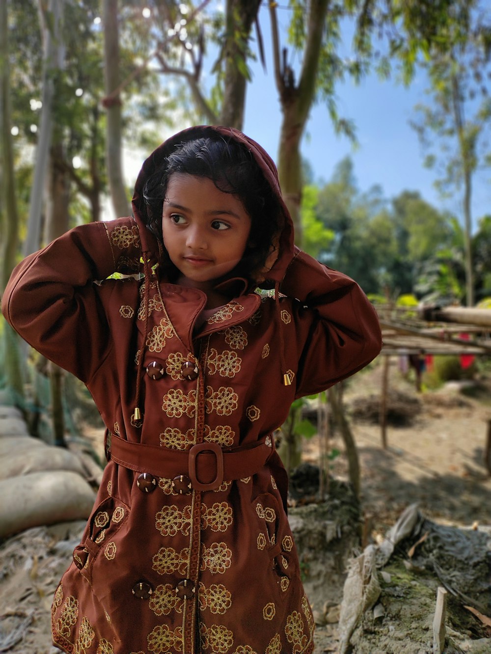 a young girl in a brown dress standing in a forest