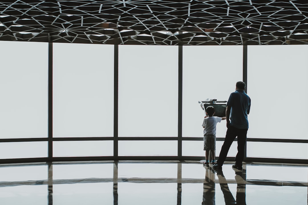 a man standing next to a little boy in front of a window, Family using a digital electronic telescope of the Burj Khalif