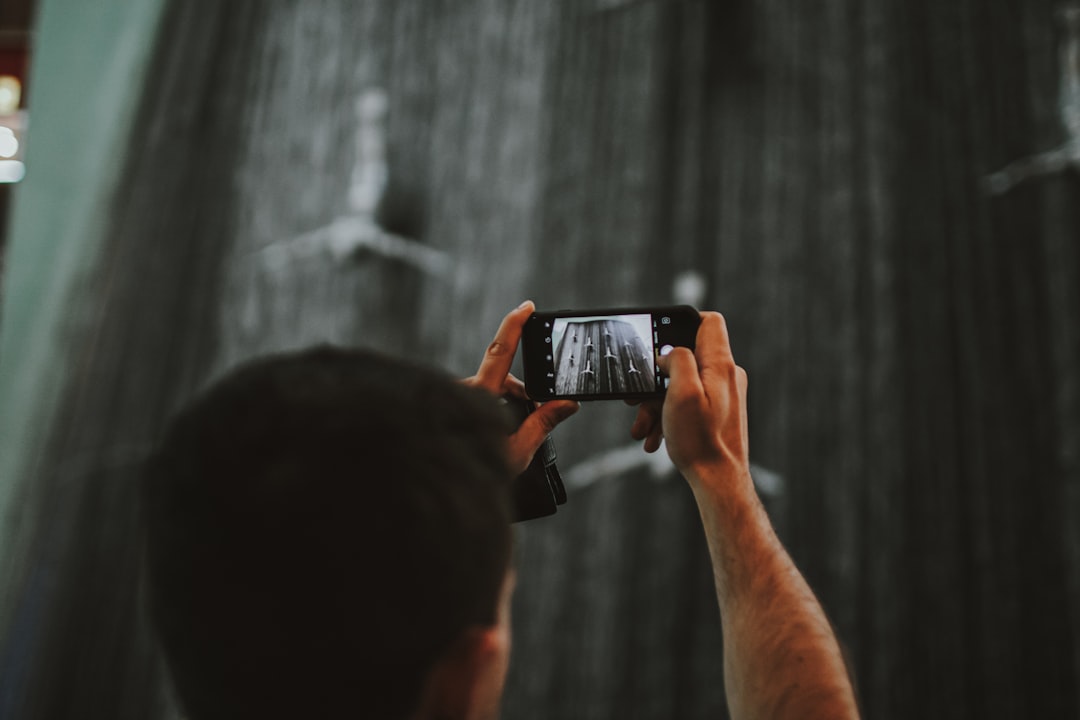 a man taking a picture of a shower with his cell phone, Person holding phone by taking pictures and videos on the modern
