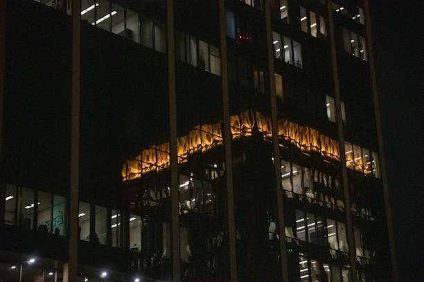 Modern office building with dark tones and subtle yellow lighting highlighting its structure at dusk.