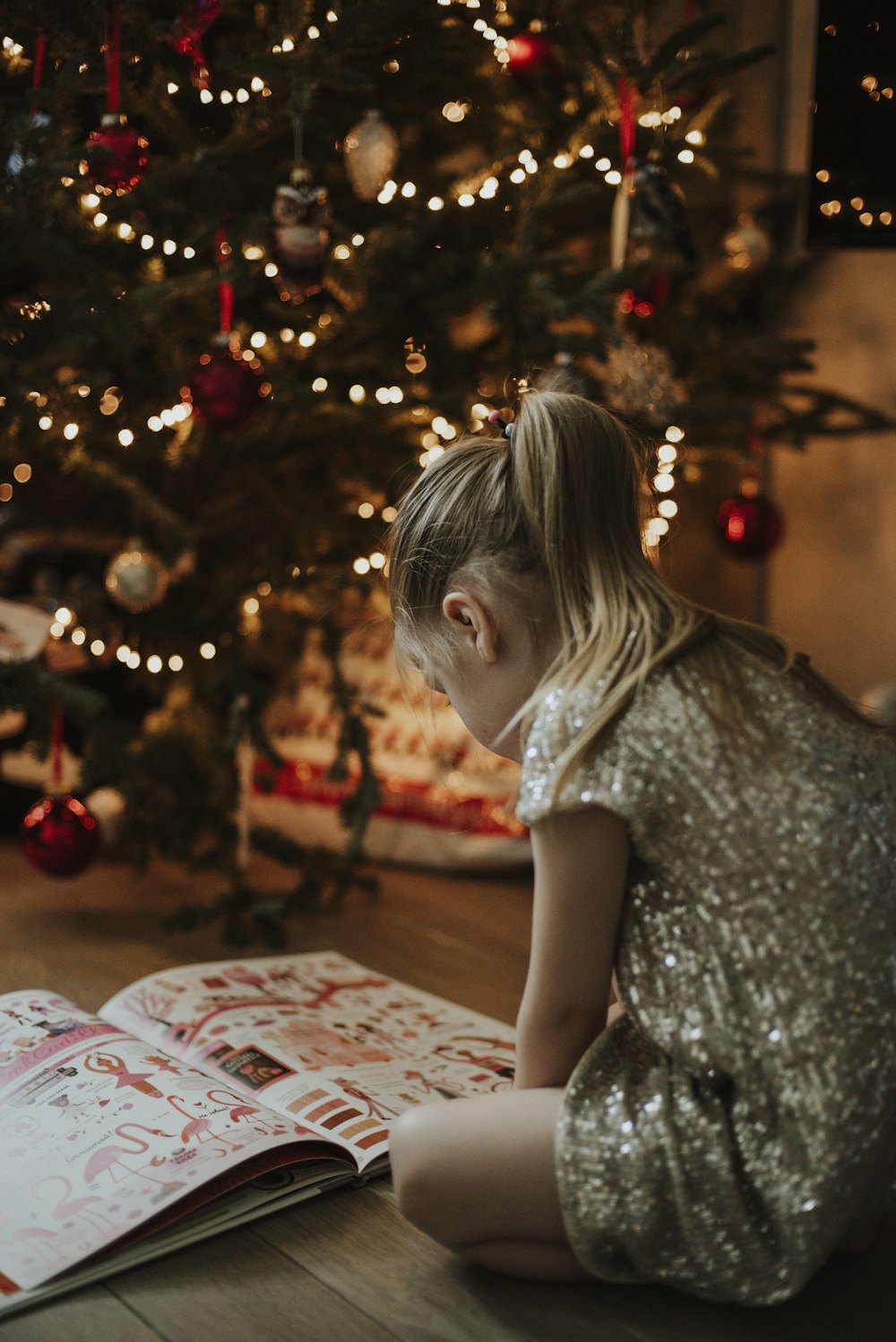 a little girl sitting on the floor reading a book