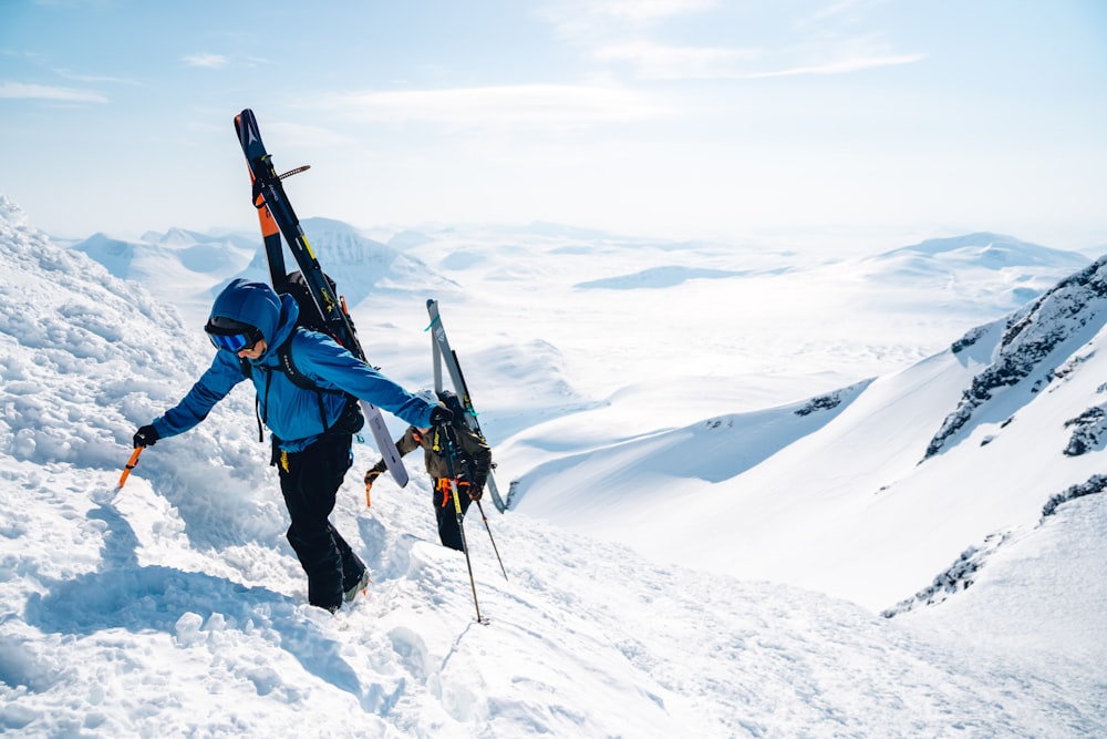 um homem subindo uma montanha coberta de neve segurando esquis